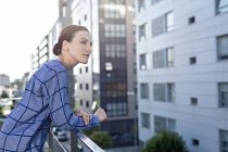 Вид сбоку женщины-менеджера в чеканной рубашке, улыбающейся и отводящей взгляд, стоя на балконе офисного здания — стоковое фото