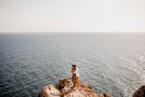 From above peaceful woman and man hugging on stone cliff above endless ocean landscape — Stock Photo