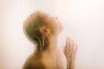 Вид збоку молодої жінки, приймаючи душ за мокру прозору перегородку у ванній — стокове фото