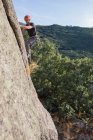 Снизу человек карабкается по скале на природе с альпинистским снаряжением — стоковое фото