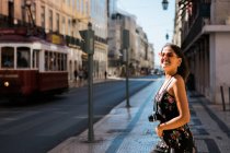 Mulher bonita confiante em vestido de verão segurando uma câmera fotográfica enquanto está em pé na pitoresca rua ensolarada da cidade em Lisboa, Portugal — Fotografia de Stock