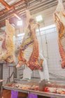 D'en bas mature carcasse de vache en bonne santé être coupé en morceaux par un boucher avec scie tout en accrochant dans l'atelier de l'abattoir — Photo de stock