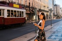 Довірлива красива жінка в літній сукні з фотокамерою, стоячи на мальовничій сонячній вулиці в Лісабоні (Португалія). — стокове фото