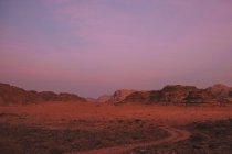 Cielo nublado violeta sobre cresta montañosa áspera y desierto de Wadi Rum por la noche en Jordania - foto de stock