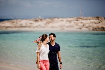 Happy couple walking on turquoise seashore in summer light — Stock Photo