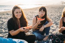 Zwei nachdenkliche Frauen am Strand essen Wassermelone — Stockfoto