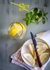 Склянка свіжого лимонаду біля тарілки з нарізаними лимонами на столі — стокове фото