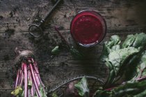 Glass of organic delicious beetroot smoothie on wooden table with raw vegetables and vintage key — Stock Photo