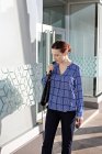 Бізнес-леді в елегантному вбранні, дивлячись вниз і стоячи на тротуарі зовні будівлі зі скляними стінами — стокове фото