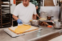 Trabalhador padaria em luvas de látex espalhando doce geléia em pão fresco sobre balcão de cozinha — Fotografia de Stock