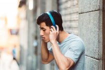 Радостный случайный азиат в наушниках, слушающий музыку, стоя на солнечной улице города — стоковое фото