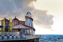 Attractions colorées du parc d'attractions sur la jetée près de la mer agitant contre le ciel nuageux dans la soirée à Brighton, Angleterre — Photo de stock