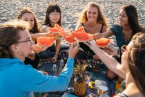A group of friends on the beach gather their pieces of watermelon — Stock Photo