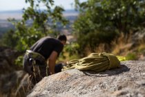 Rope on rock with defocused climber on the background preparing his equipment to start climbing — Stock Photo