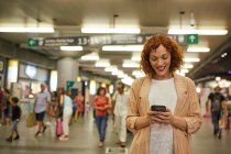 Rothaarige junge Frau nutzt Smartphone am Bahnhof — Stockfoto