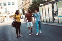 Happy carefree people in casual clothes embracing and strolling together along urban street — Stock Photo