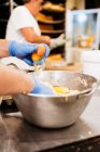 Pastelero de cosecha en guantes y mezcla uniforme y amasar masa fresca suave mientras se prepara la pastelería en la panadería - foto de stock