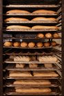 Mains de pain frais délicieux et petits pains placés sur des plateaux métalliques sur un rack dans une boulangerie — Photo de stock