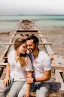 Щасливі коханці сидять на зруйнованому причалі на березі моря — стокове фото