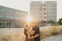 Вид збоку на романтичну пару, що зв'язується і цілується по дорозі вздовж міської будівлі на сонячному світлі — стокове фото