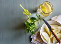 Bicchiere di limonata fresca accanto al piatto con limoni tagliati sul tavolo — Foto stock