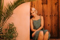 Junge Frau mit geschlossenen Augen sitzt neben Holztür und Pflanzen im Hof — Stockfoto
