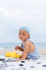 Vista trasera de un bebé con una gorra en la playa junto a sus patos de goma - foto de stock
