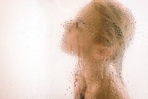 Vista lateral da jovem mulher tomando banho atrás da divisória transparente molhada no banheiro — Fotografia de Stock