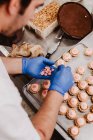 De dessus confiseur méconnaissable décorer pâtisserie rose sur plateau tout en travaillant dans la boulangerie — Photo de stock