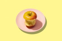 Свежее укушенное яблоко в тарелке на желтом фоне. Яркий красочный узор — стоковое фото
