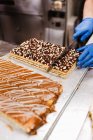 Erntehelfer in Uniform und Handschuhen schneidet in Bäckerei süßen frischen Kuchen auf den Tisch — Stockfoto