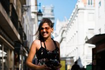 Verspielte Frau im langen Kleid hält eine Fotokamera in der Hand, während sie durch die Sommerstraße der Stadt läuft — Stockfoto