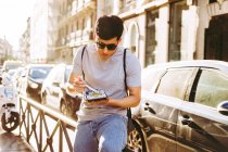 Schöner asiatischer Mann mit Sonnenbrille isst Essen zum Mitnehmen mit Essstäbchen, während er neben einem Foodtruck auf der sonnigen Straße steht — Stockfoto