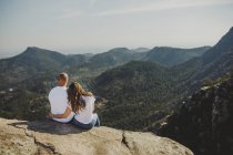 Feliz pareja sentada en el acantilado de las montañas - foto de stock
