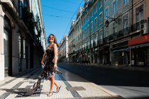 Грайлива жінка в довгій сукні обертається під час прогулянки по міській літній вулиці — стокове фото