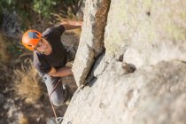 Сверху человек карабкается по скале на природе с альпинистским снаряжением — стоковое фото