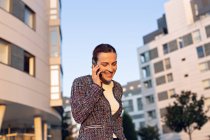 Allegro imprenditrice sorridente e distogliendo lo sguardo mentre parla su smartphone e in piedi sulla strada — Foto stock