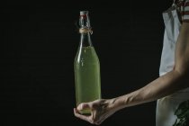Mano femenina con botella de sidra de saúco - foto de stock