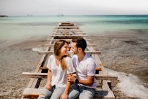 Счастливые влюбленные сидят на разрушенном пирсе на берегу моря — стоковое фото