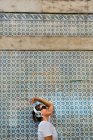 Bella donna spensierata in abito casual e cuffie in piedi sul muro di mosaico blu di costruzione sulla strada della città — Foto stock