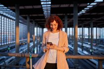 Улыбающаяся молодая женщина просматривает телефон на станции — стоковое фото