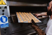 Crop man espiando dentro del horno profesional mientras trabaja en la panadería - foto de stock