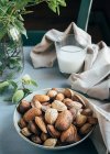 Склянка білого мигдалевого молока поруч з мигдалем в мушлях і зелених гілочках на кухонному столі — стокове фото