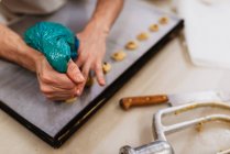 Анонимный повар, сжимающий свежее тесто на подносе бумагой, работая на размытом фоне пекарни — стоковое фото