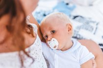 Portrait of a blonde baby with a pacifier taken with his mother before going to sleep — Stock Photo