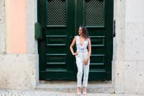 Modern beautiful woman in trendy outfit standing beside doorway of building on scenic street — Stock Photo