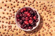 Vista dall'alto di ciliegie dolci fresche in ciotola con semi di ciliegia intorno sul tavolo di legno — Foto stock