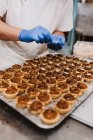 Homem irreconhecível em luvas de látex colocando nozes em cima de bolos pequenos doces enquanto trabalhava na padaria — Fotografia de Stock