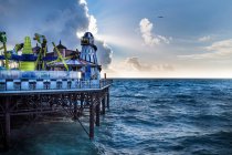 Atrações coloridas de parque de diversões no cais perto do mar acenando contra o céu nublado à noite em Brighton, Inglaterra — Fotografia de Stock