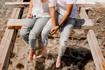 Обрезанный образ влюбленных, сидящих на разрушенном пирсе на берегу моря — стоковое фото